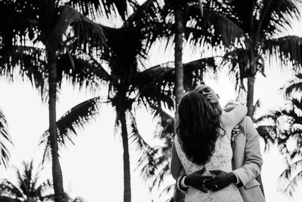 Romantic black and white wedding portrait of couple embracing under palm trees in Cancun Riviera Maya Mexico