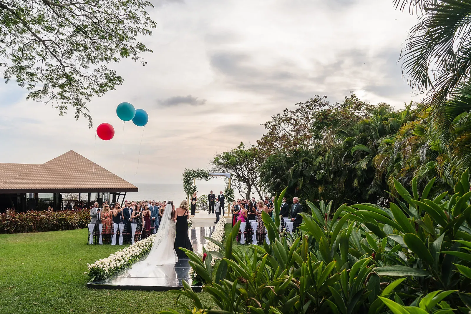 bride walking down the isle in a beautiful scenario at sunset with balloons blowing in the wind
