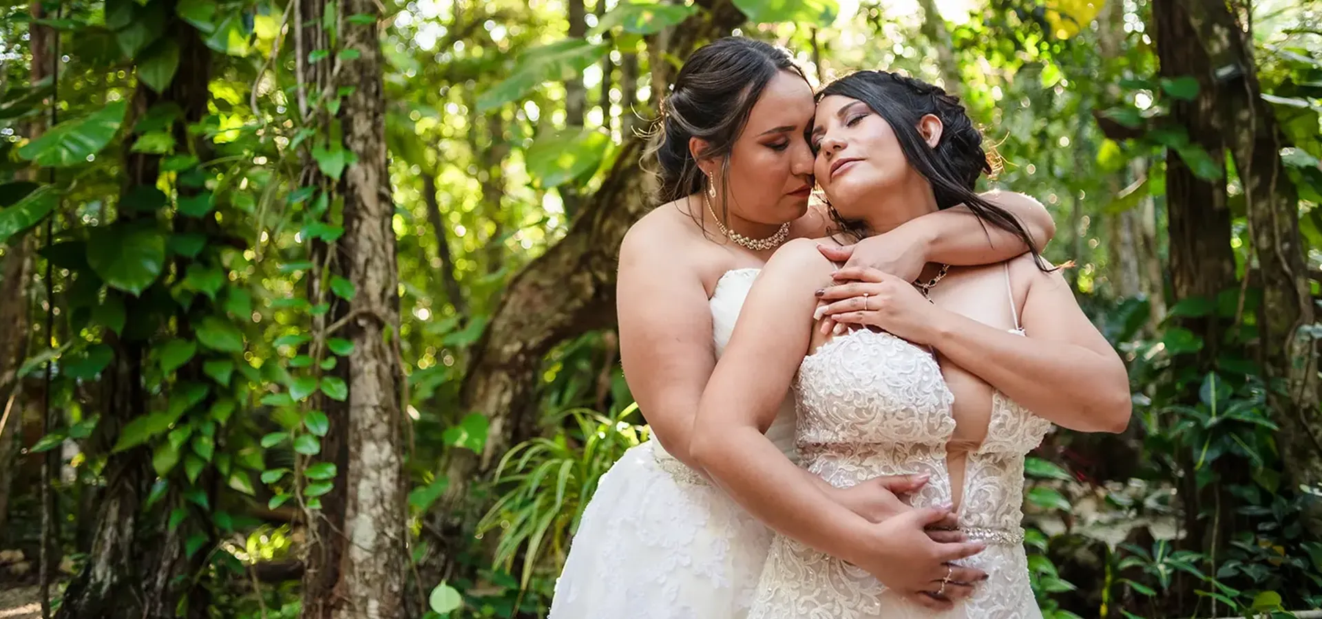 Two brides embracing in lush tropical jungle setting for romantic wedding photography session in Riviera Maya Mexico