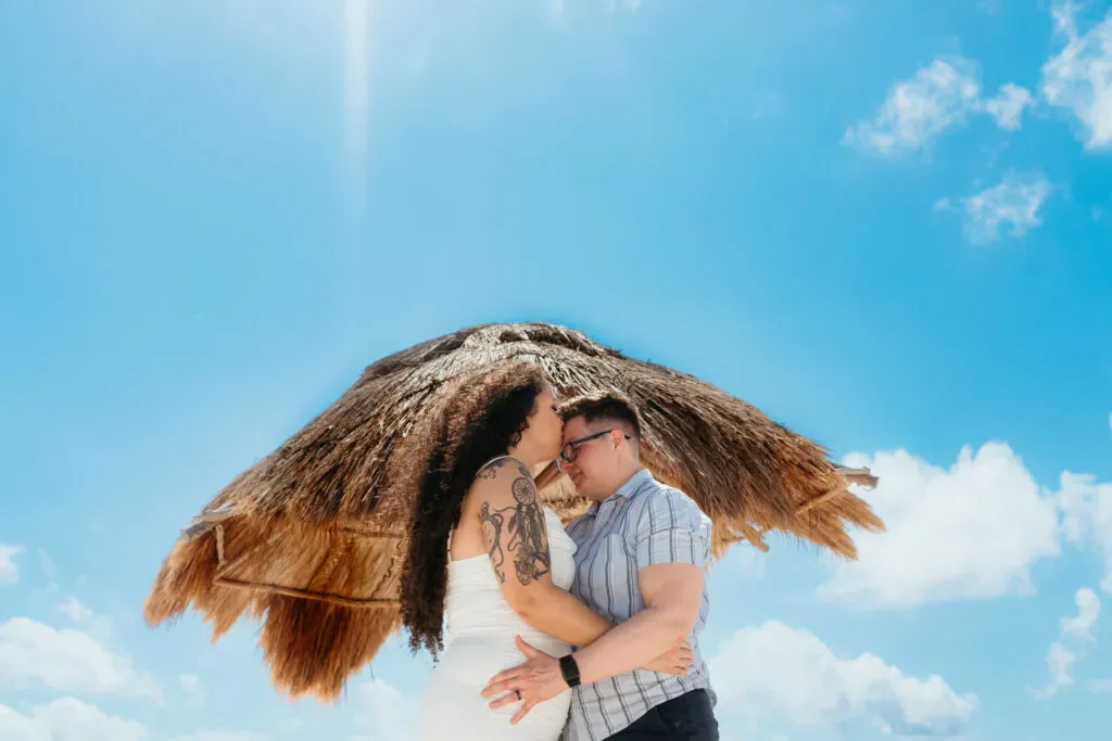 Romantic couple embracing under thatched palapa umbrella in Cancun Mexico destination wedding engagement photography session