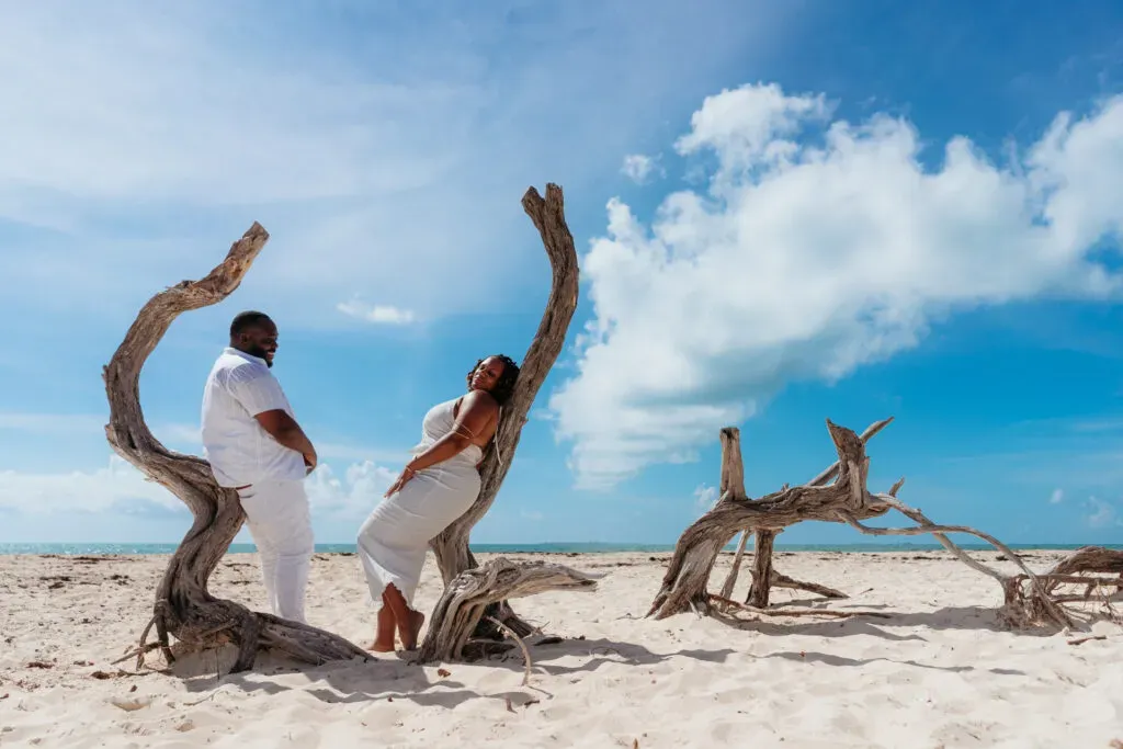 Romantic couple in white outfits posing on driftwood at Cancun beach for engagement photoshoot in Riviera Maya Mexico