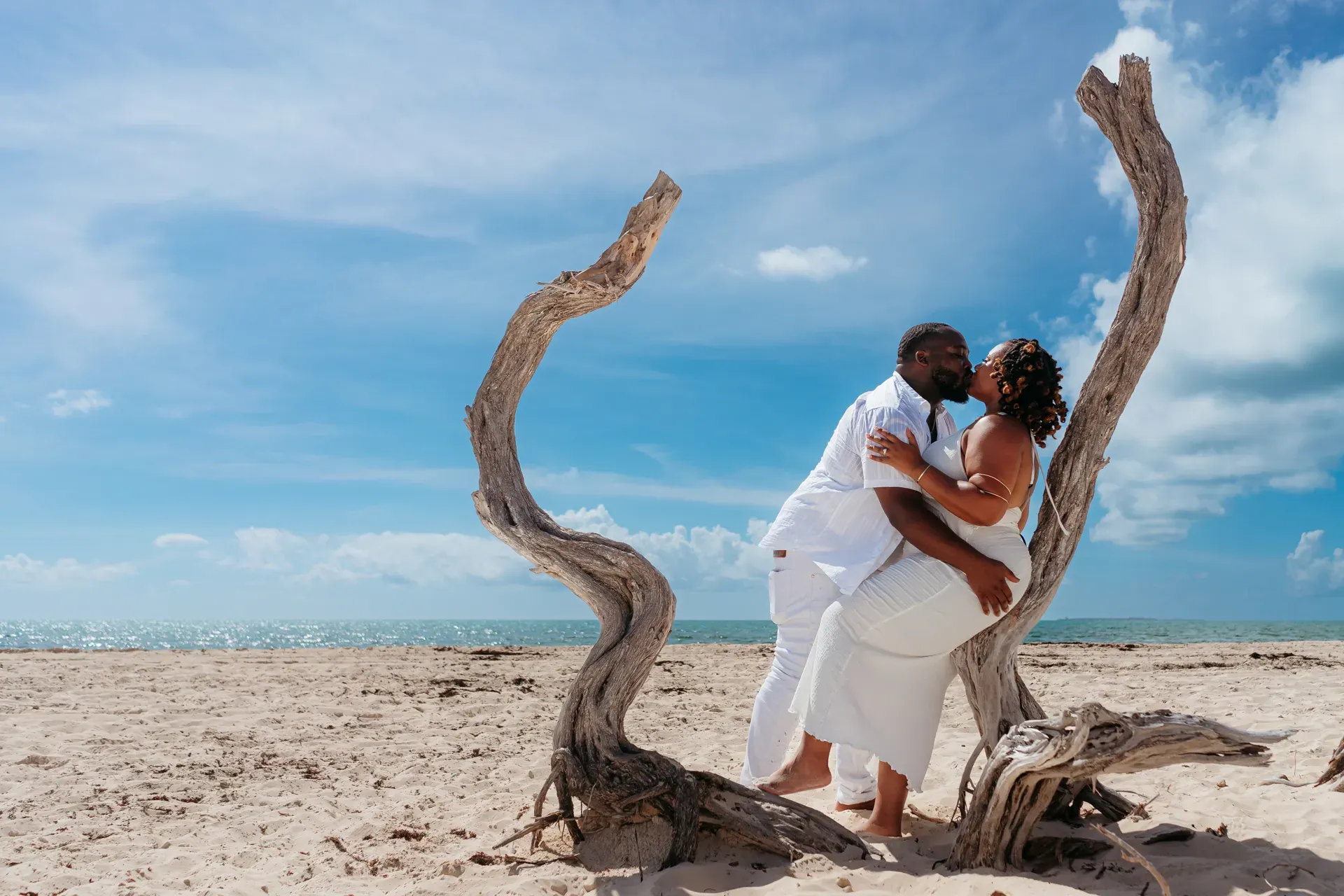 Romantic kiss under driftwood arches in Isla Blanca, Cancun engagement photographer