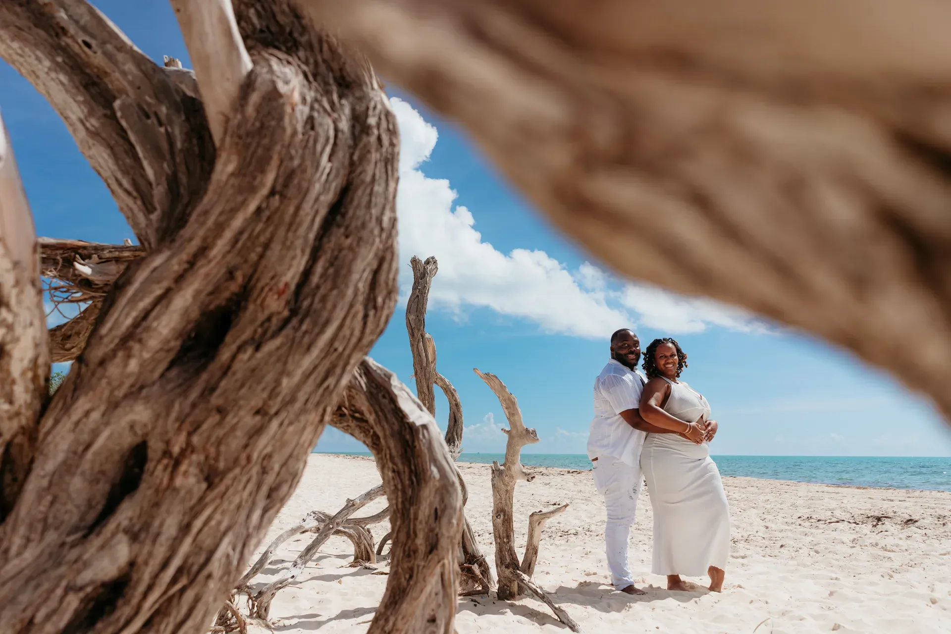 Couple framed by driftwood during engagement photo session in Isla Blanca, Cancun