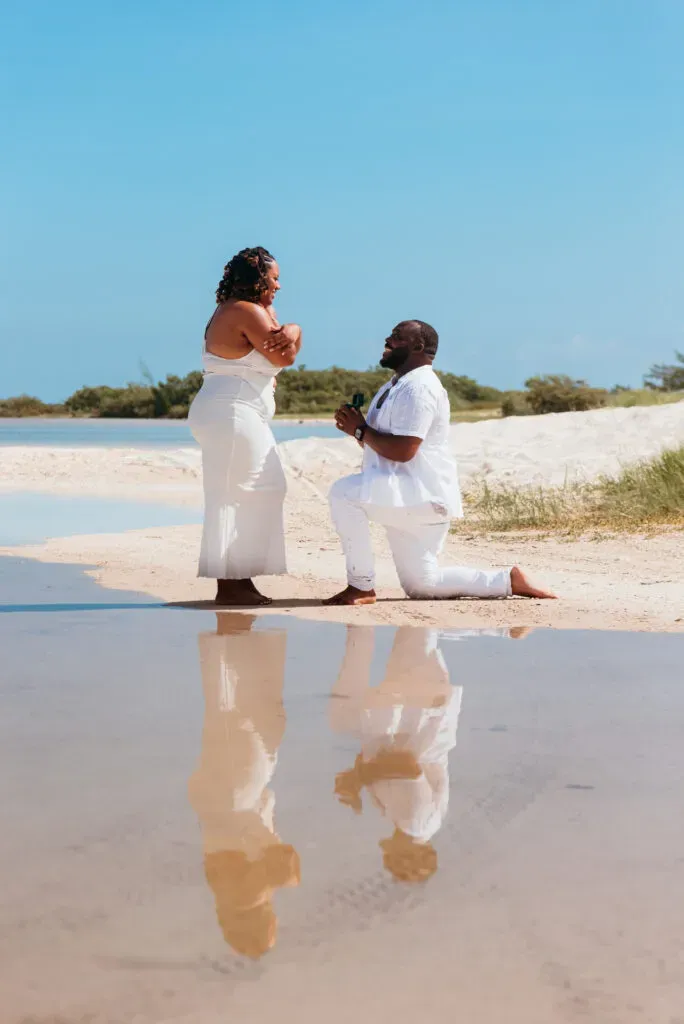 Beach proposal in Cancun - man kneeling with ring as woman reacts with joy on pristine Riviera Maya sand with water reflection