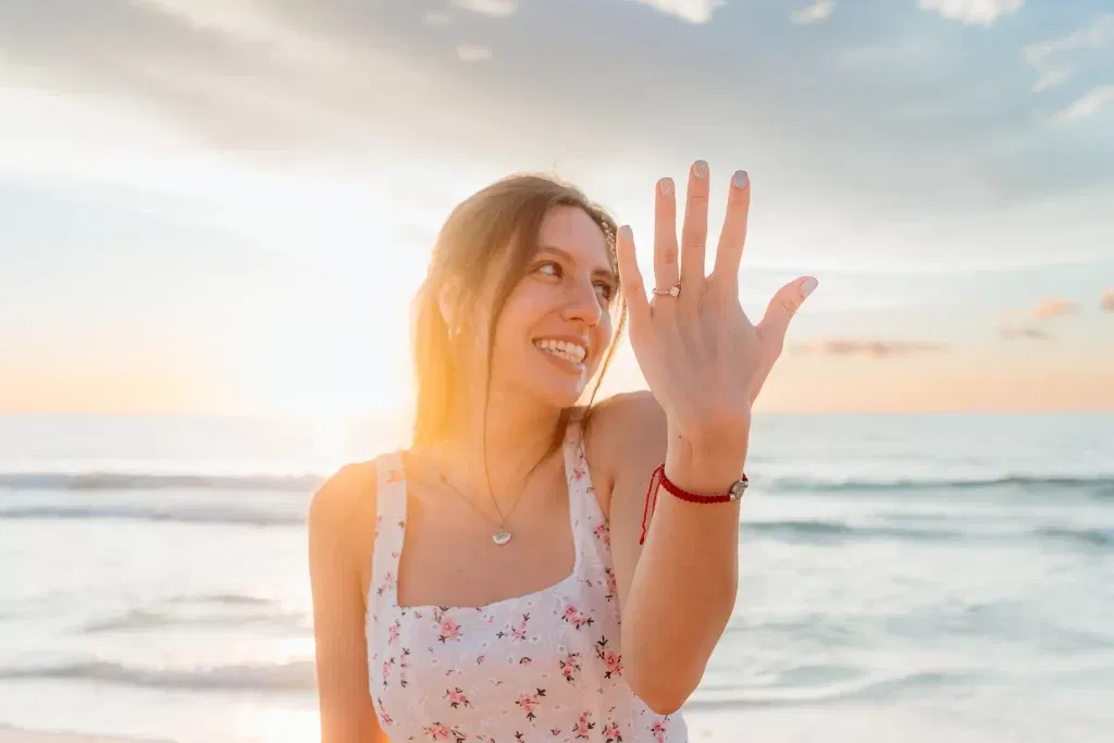 Bride waving at sunset beach in Cancun showing engagement ring during romantic couples photography session Riviera Maya