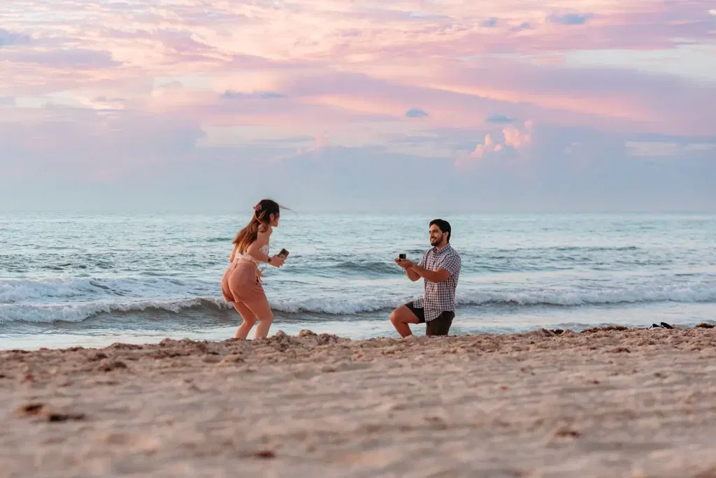 Surprise beach proposal at sunrise in Cancun with partner kneeling as other reacts with joy on Caribbean sand