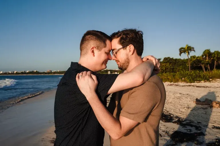 Gay couple embracing on Cancun beach during golden hour engagement photoshoot in Riviera Maya Mexico