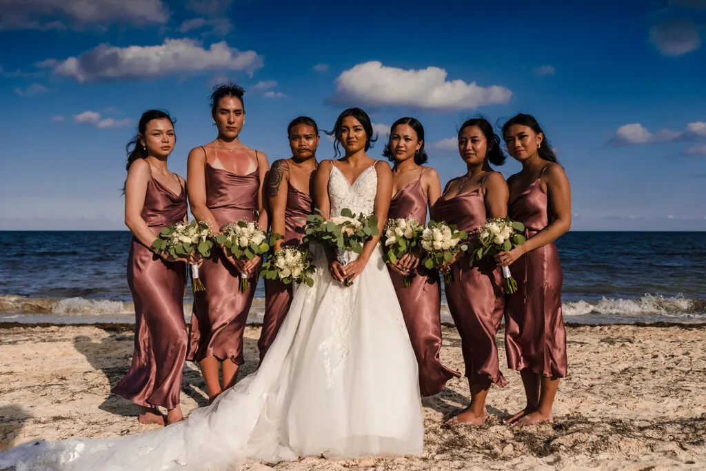 Bride with bridesmaids in rose gold dresses holding bouquets on Cancun beach - destination wedding photography Riviera Maya