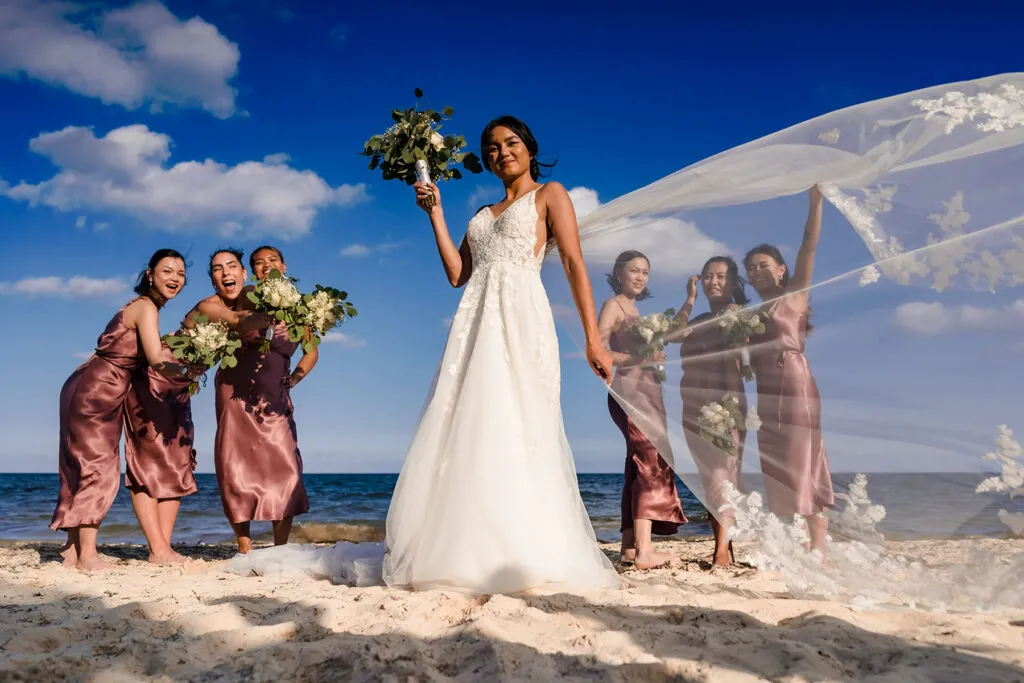 Bride with bouquet and bridesmaids in rose gold dresses at beach wedding ceremony in Cancun Riviera Maya Mexico