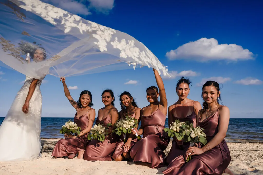 Beach wedding photography Cancun bride with bridesmaids in rose gold dresses holding bouquets on Riviera Maya sand