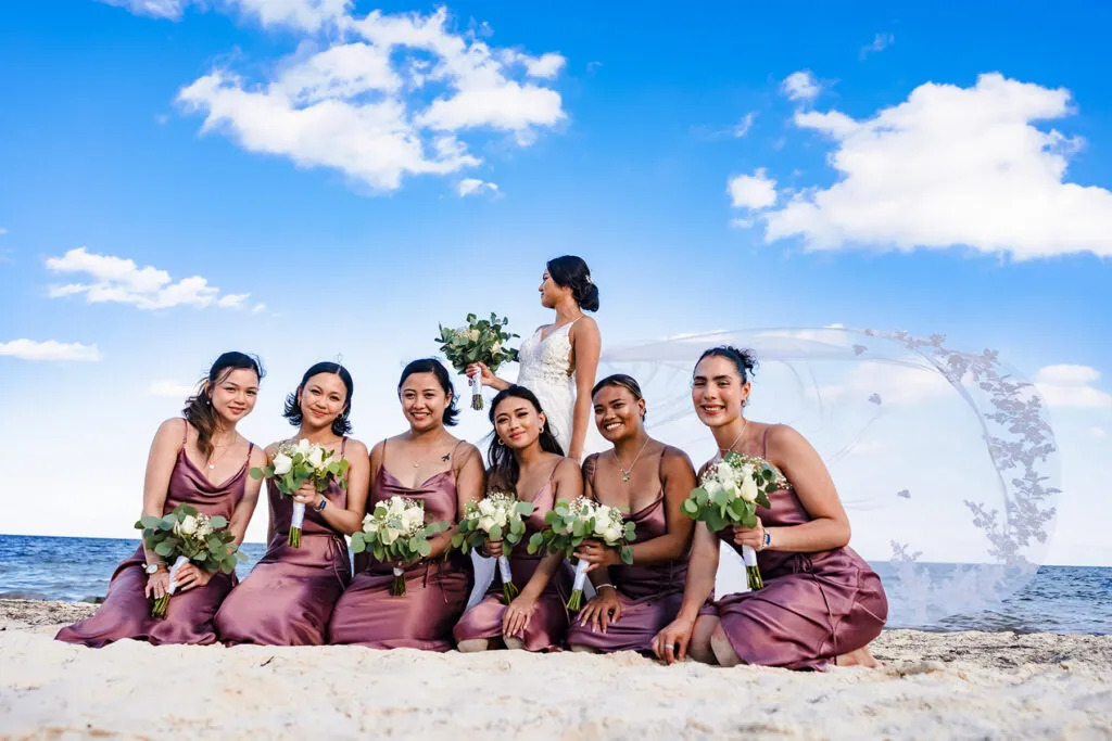 Bride and bridesmaids in purple dresses with bouquets on Cancun beach - destination wedding photography Riviera Maya
