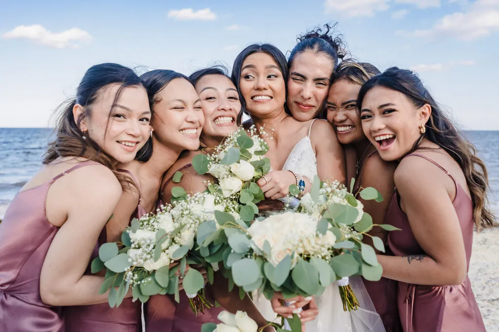 Bride with bridesmaids holding bouquets on Cancun beach - destination wedding photography in Riviera Maya Mexico