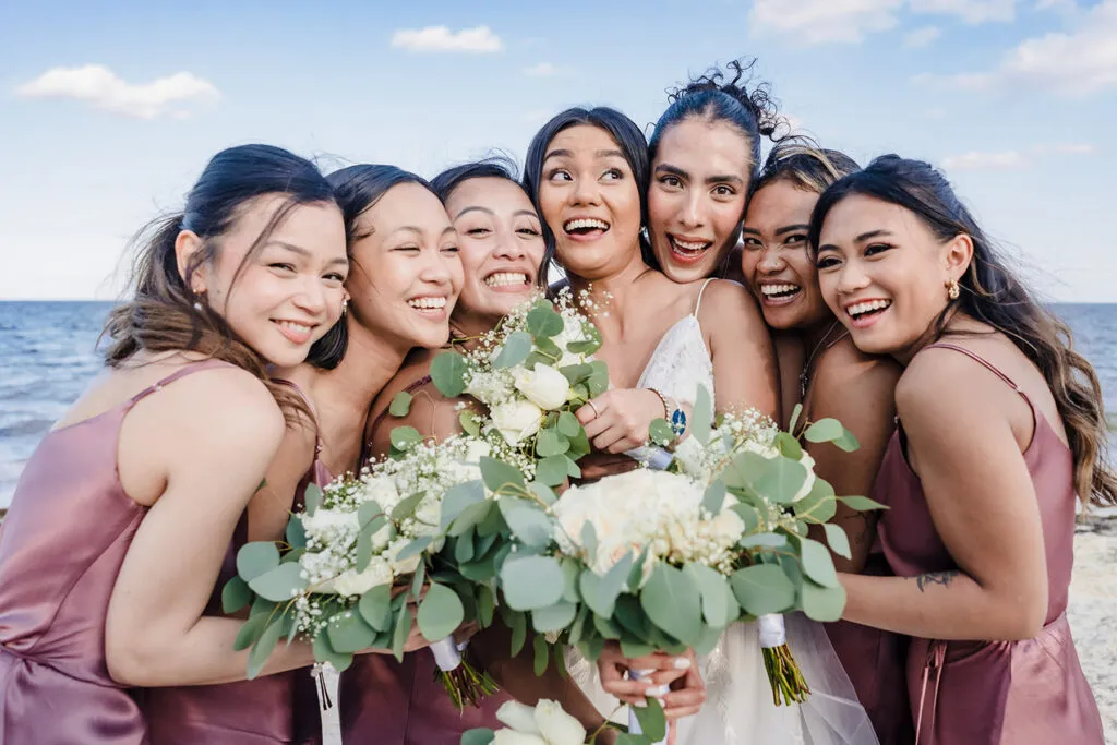Bride and bridesmaids celebrate beach wedding in Cancun with white rose bouquets and ocean backdrop in Riviera Maya Mexico