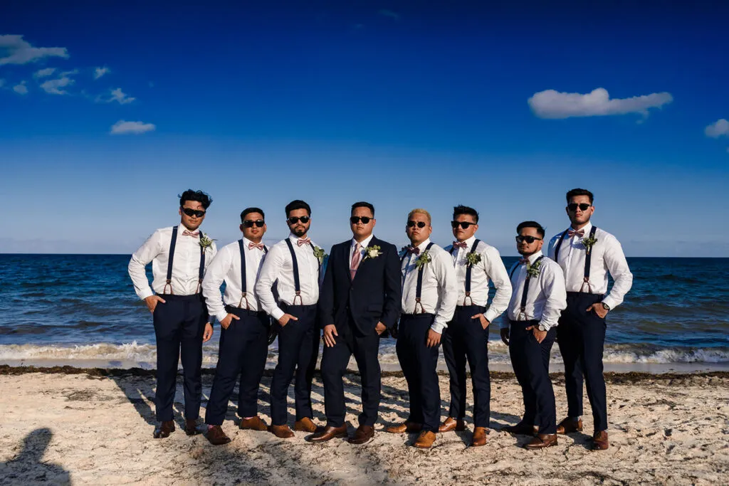 Groom and groomsmen in navy suits and suspenders posing on Cancun beach for destination wedding photography