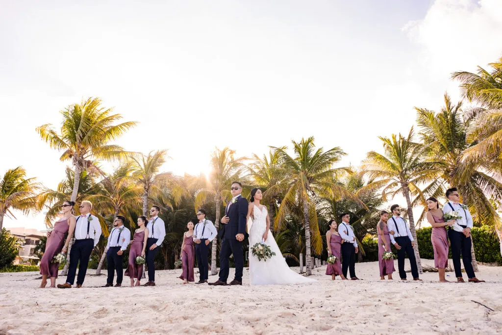Beach wedding party poses on white sand with palm trees at sunset in Cancun Riviera Maya Mexico destination wedding photography