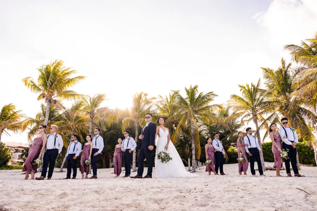 Beach wedding party in Cancun with bride, groom and bridal party posing among palm trees at tropical Riviera Maya resort