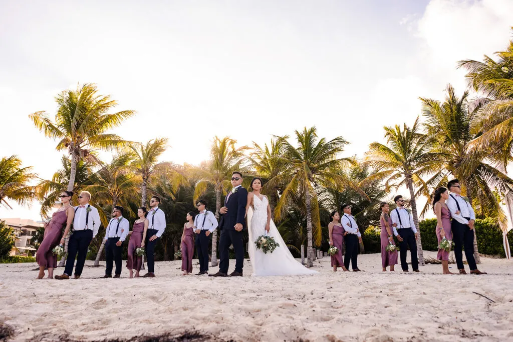 Beach wedding party photo at sunset with bride, groom and wedding party on Riviera Maya sand with palm trees in Cancun Mexico