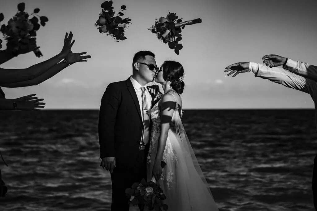 Romantic black and white wedding photo of bride and groom kissing with flower petals falling in Cancun Riviera Maya Mexico