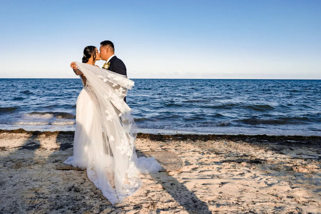 Romantic bride and groom kissing on pristine beach in Cancun Mexico during golden hour wedding photography session
