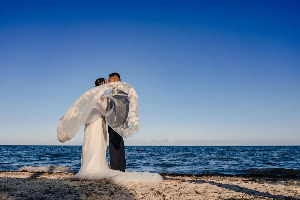 Bride and groom embracing on beach with flowing veil in Cancun Mexico destination wedding photography session