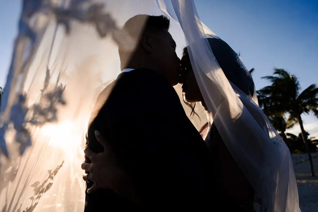 Romantic silhouette of bride and groom embracing under flowing veil at sunset wedding in Cancun Riviera Maya Mexico