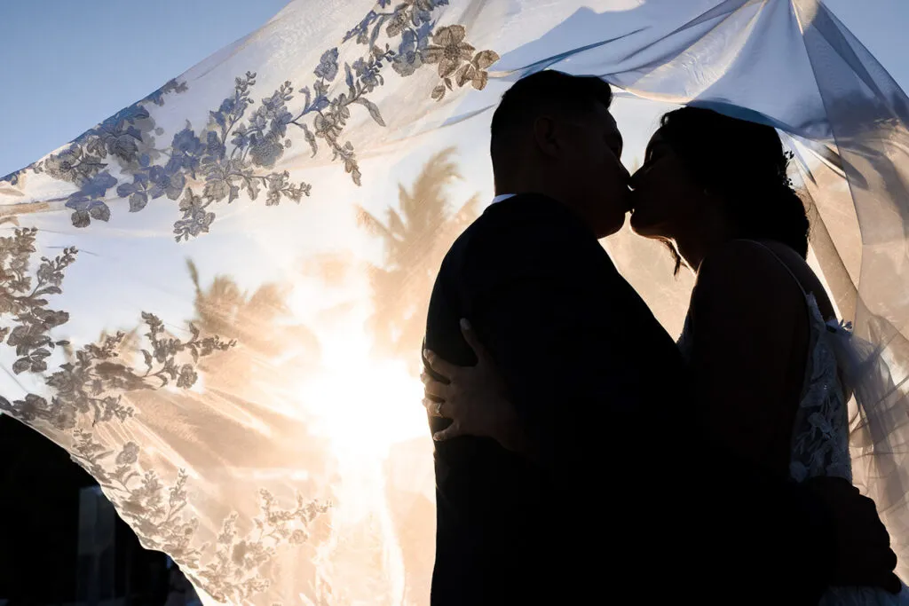 Romantic couple silhouette kissing under floral canopy at golden hour wedding ceremony in Cancun Riviera Maya Mexico