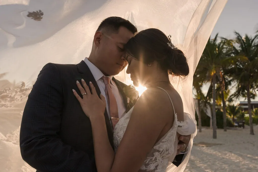Romantic bride and groom embrace at sunset wedding ceremony in Cancun Riviera Maya Mexico with palm trees and beach backdrop