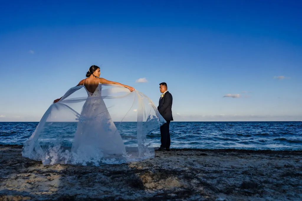 Bride in flowing white dress and groom on Cancun beach at sunset - romantic Riviera Maya wedding photography session