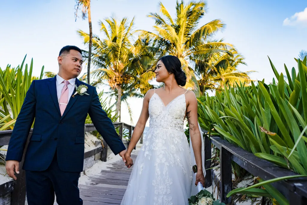 Bride and groom walking hand in hand through tropical palm trees at their Cancun Riviera Maya beach wedding photography session