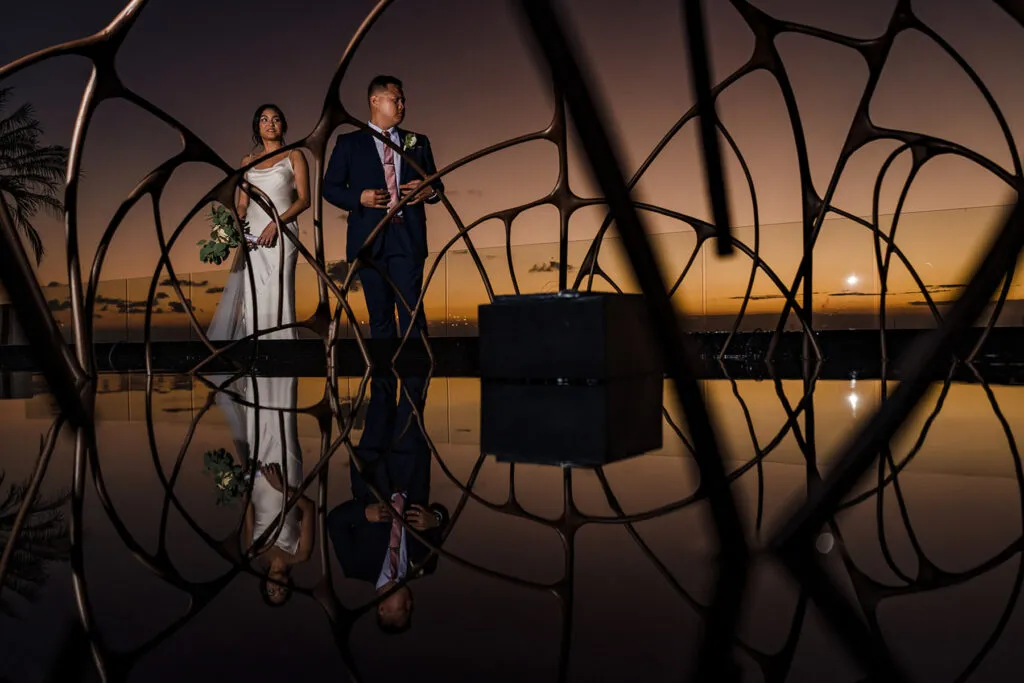 Bride and groom sunset portrait through decorative metalwork at luxury Cancun resort wedding venue in Riviera Maya Mexico