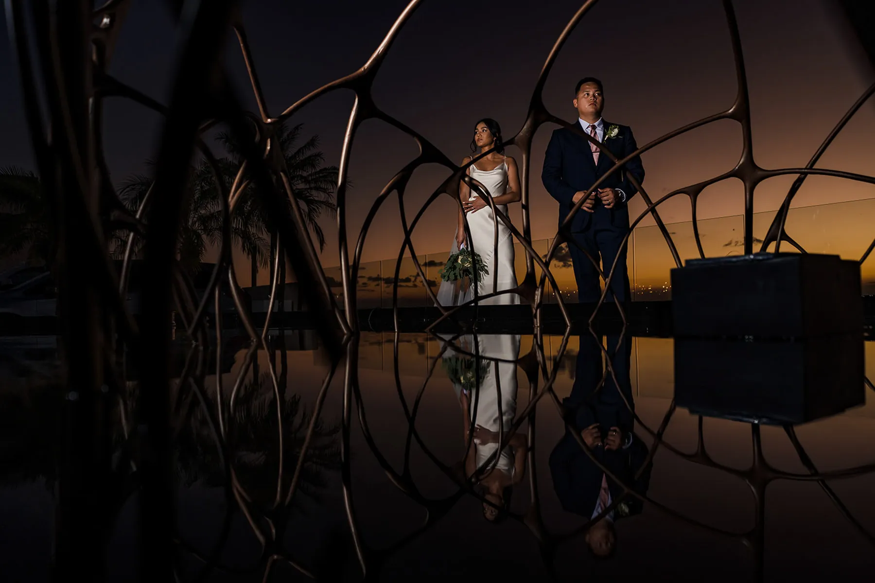 Bride and groom sunset portrait with modern sculpture reflection at luxury Cancun wedding venue in Riviera Maya Mexico