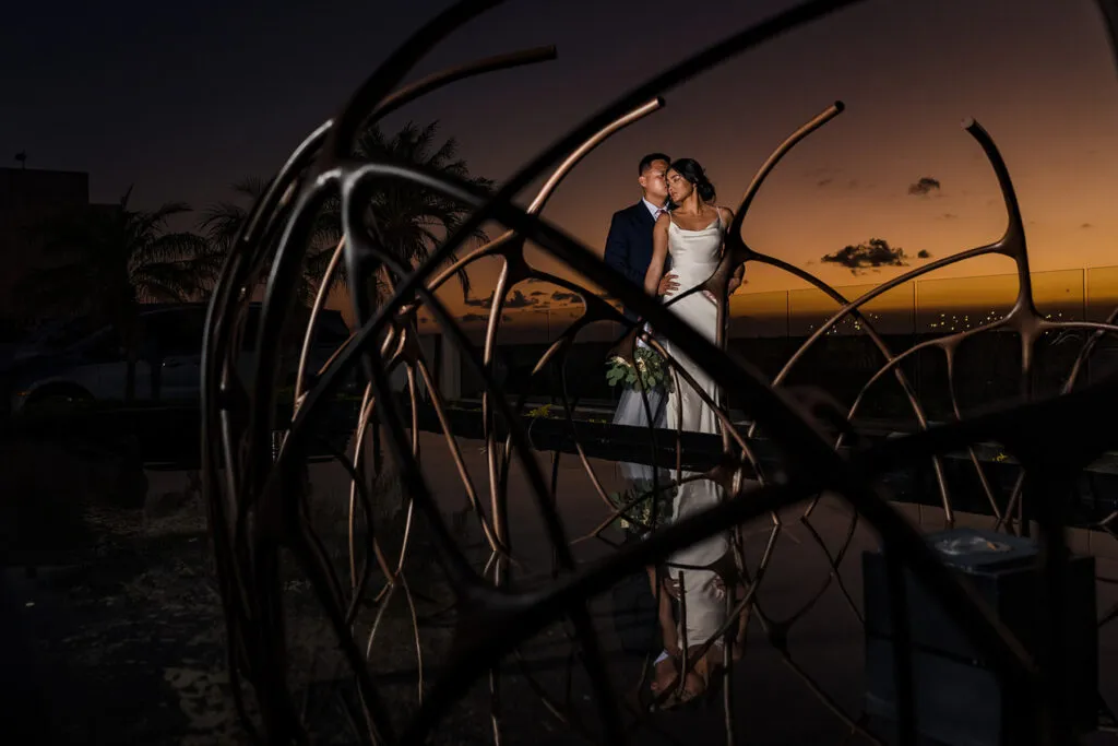 Romantic wedding couple portrait at sunset in Cancun with modern sculpture and golden sky backdrop in Riviera Maya Mexico