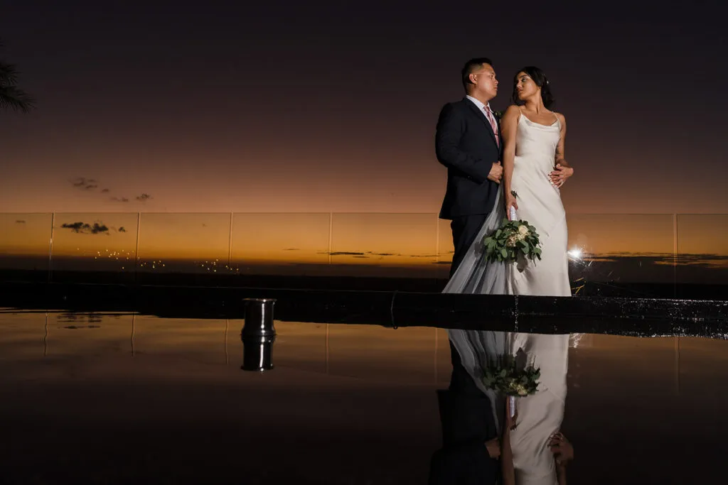 Romantic sunset wedding portrait of bride and groom embracing by infinity pool in Cancun Riviera Maya Mexico