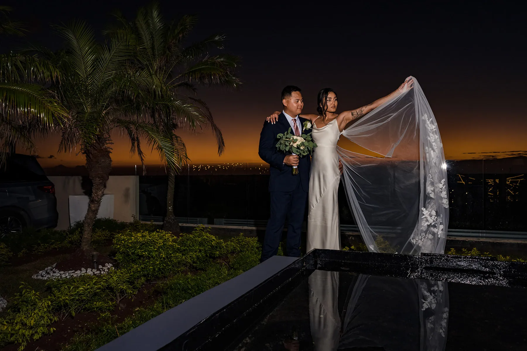 Romantic sunset wedding portrait of bride and groom by pool with palm trees in Cancun Riviera Maya Mexico destination wedding