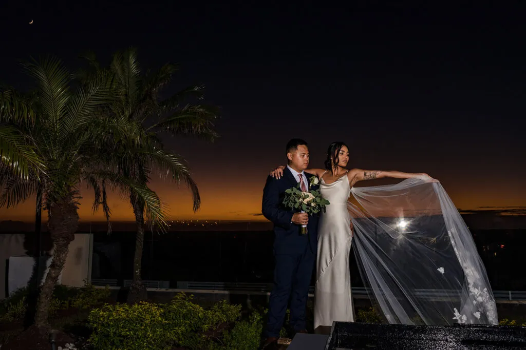 Bride and groom romantic sunset portrait with palm trees at luxury Cancun Riviera Maya wedding venue with dramatic veil