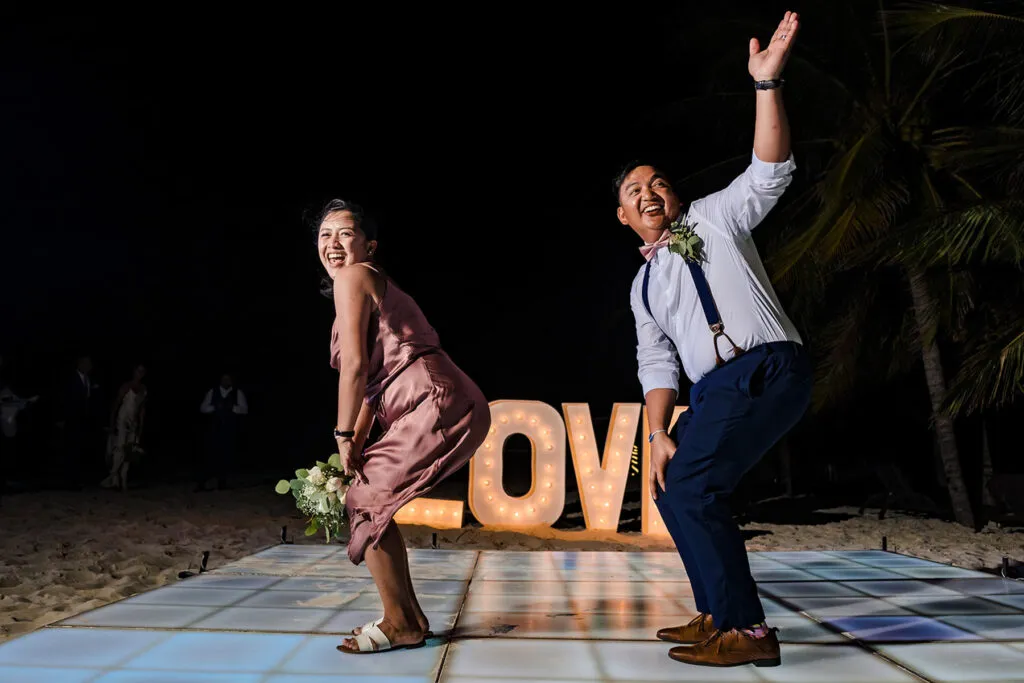 Happy newlyweds celebrating on beach dance floor with LOVE sign at tropical Cancun Riviera Maya destination wedding at night