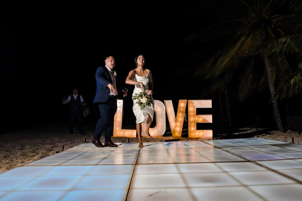 Bride and groom dancing on beach dance floor with illuminated LOVE sign at night wedding in Cancun Riviera Maya Mexico