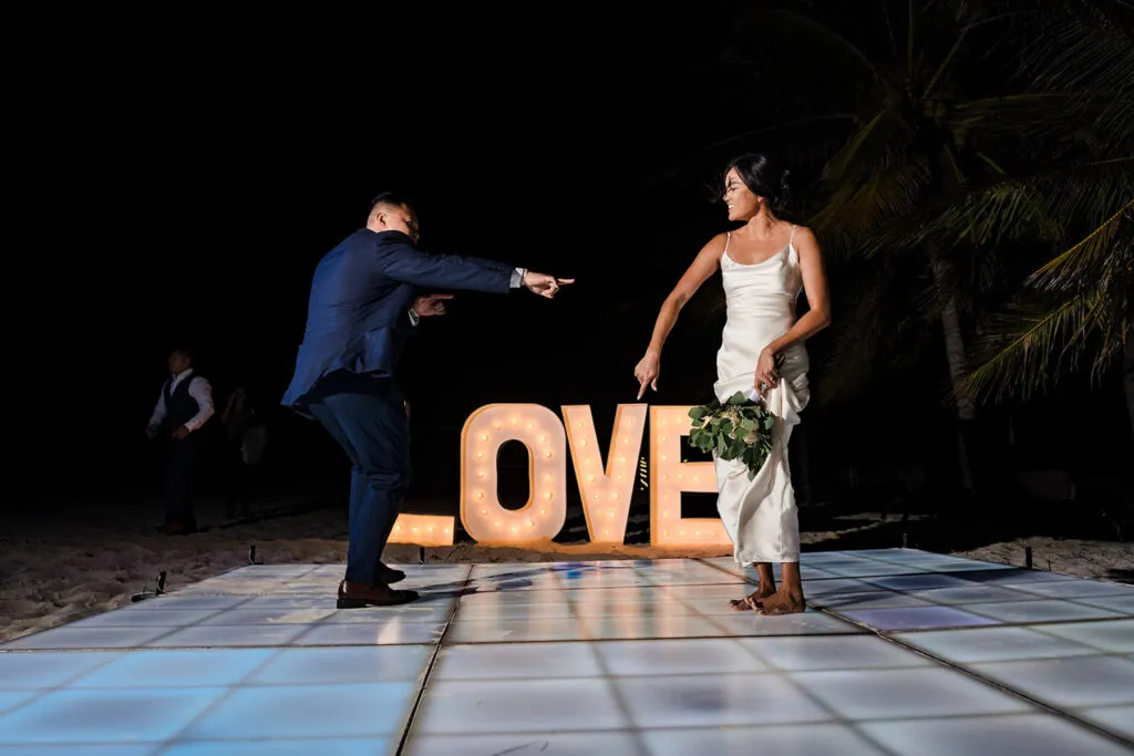 Bride and groom dancing on illuminated dance floor with LOVE sign at tropical Cancun beach wedding reception at night