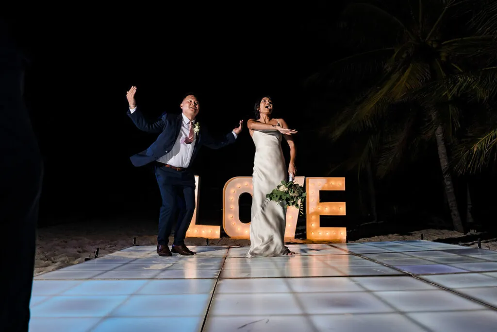 Bride and groom celebrating at night beach wedding reception with LOVE sign in Cancun Riviera Maya Mexico