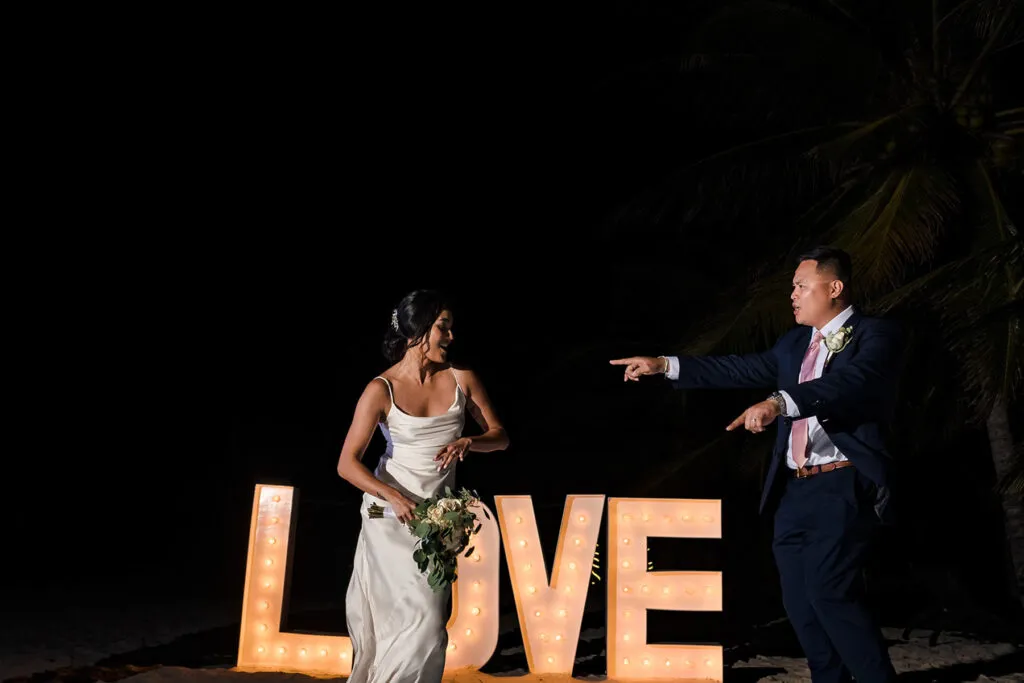 Bride and groom dancing at night by illuminated LOVE sign at Riviera Maya destination wedding in Mexico