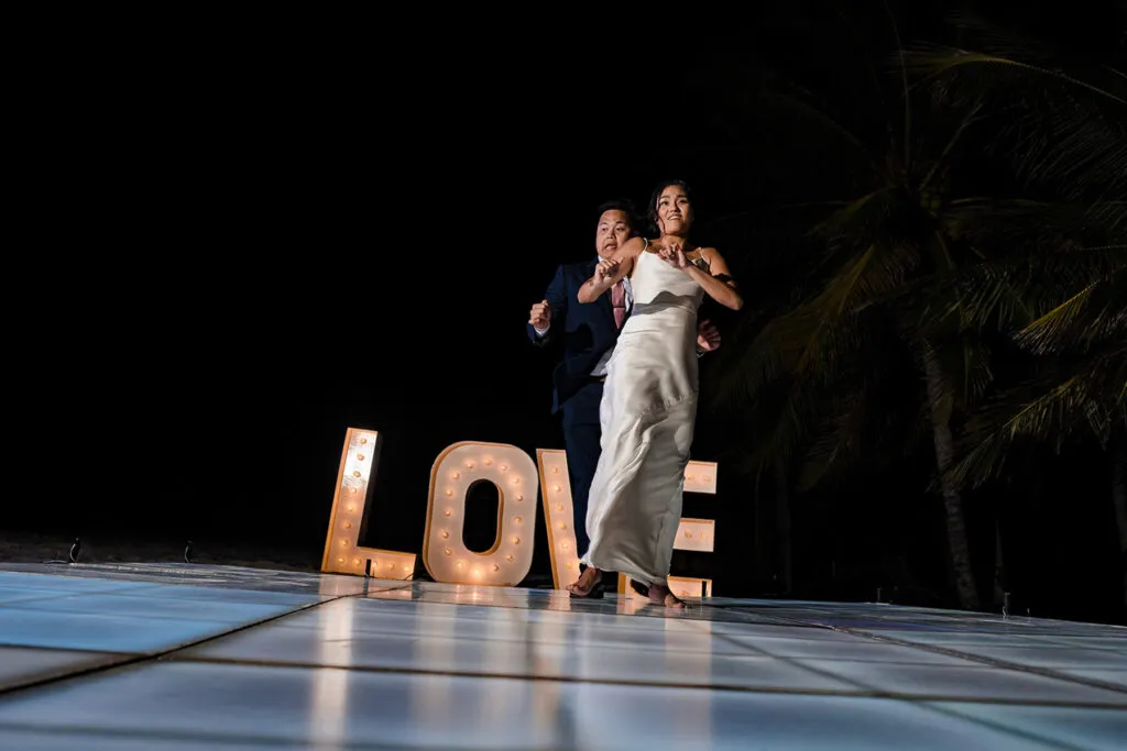 Bride and groom dancing at night wedding reception in Cancun with illuminated LOVE sign and palm trees