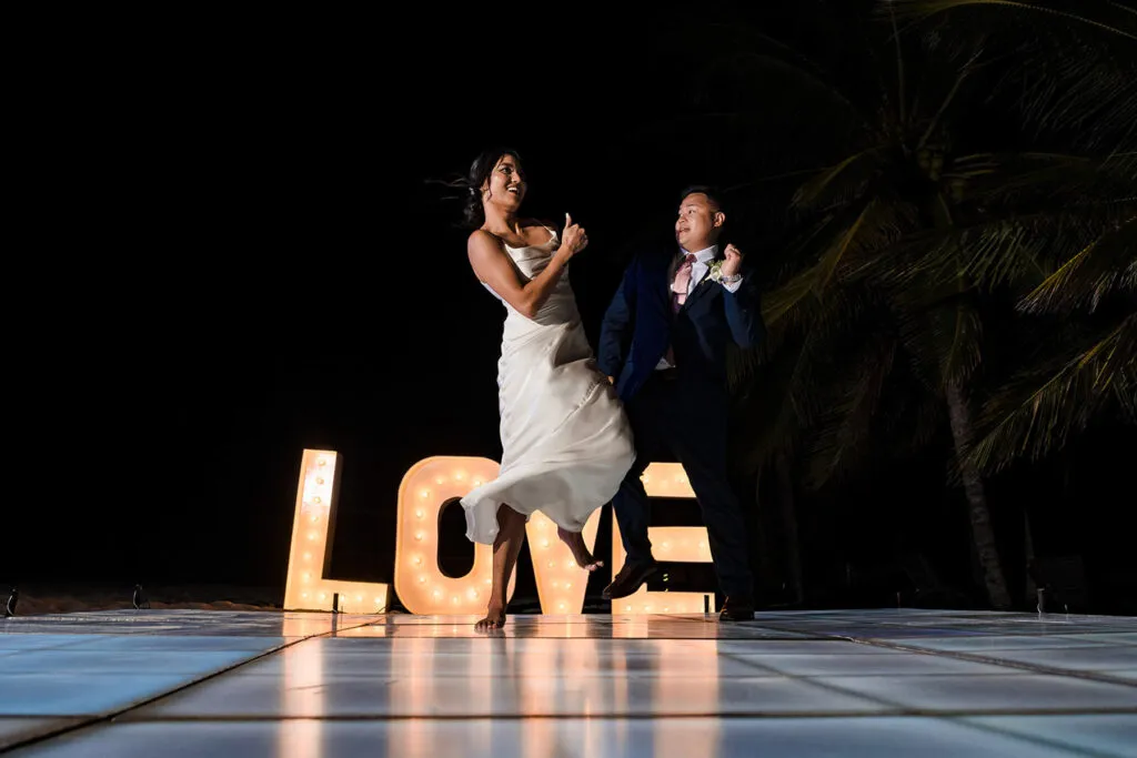 Bride and groom dancing at night wedding reception in Cancun with illuminated LOVE sign and palm trees in background