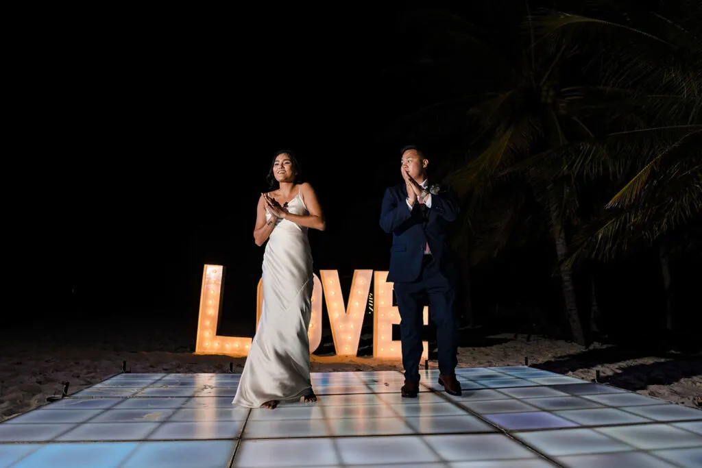 Bride and groom dancing on illuminated dance floor with LOVE sign at night beach wedding in Cancun Riviera Maya Mexico