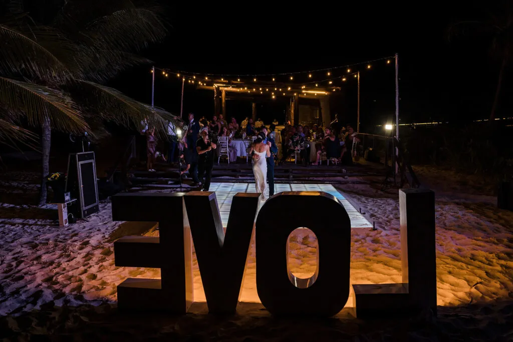 Beach wedding reception at night in Cancun with couple dancing under string lights and illuminated LOVE sign on sand