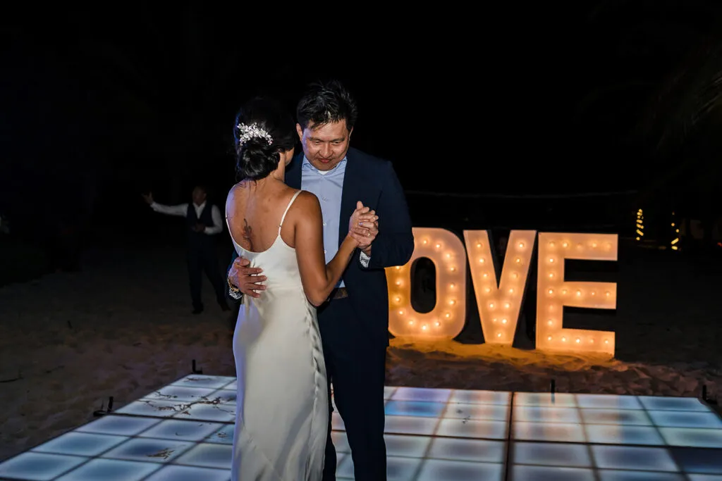 Bride and groom first dance at night wedding reception in Riviera Maya with illuminated LOVE sign backdrop