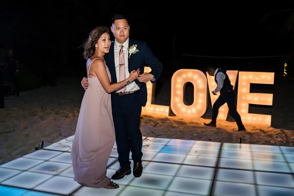 Romantic couple dancing at beach wedding reception in Cancun with illuminated LOVE sign and LED dance floor at night