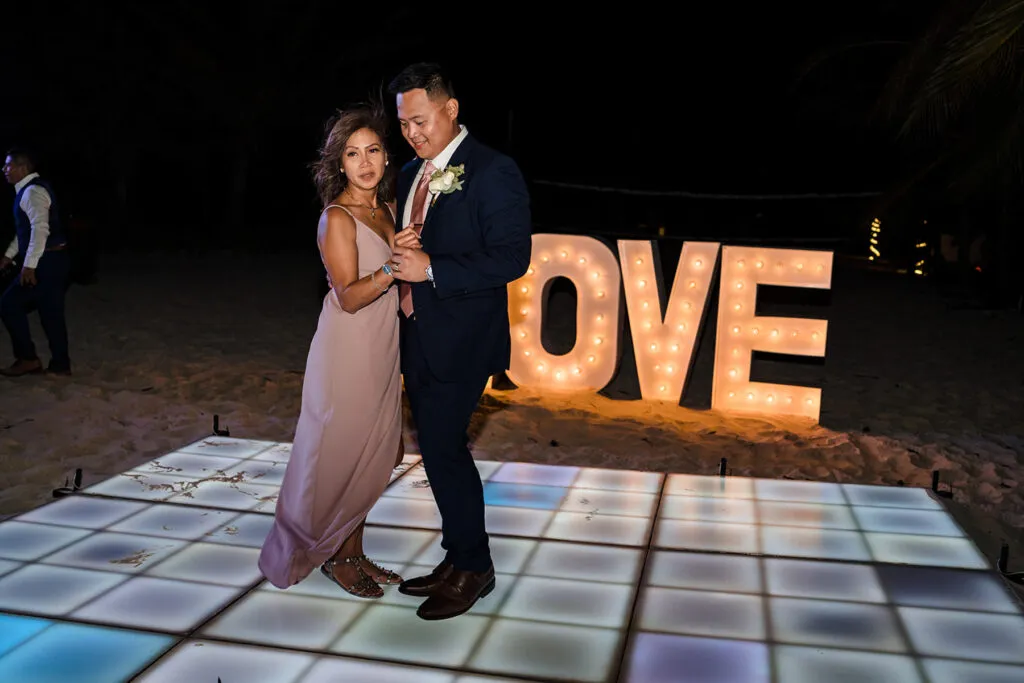 Romantic couple dancing on LED floor at beachfront wedding reception in Cancun with illuminated LOVE letters backdrop