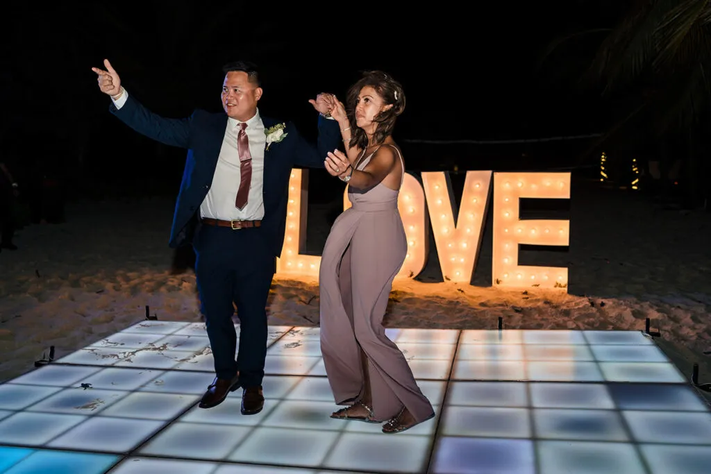Couple dancing on illuminated dance floor at beach wedding in Cancun with LOVE marquee lights backdrop at night