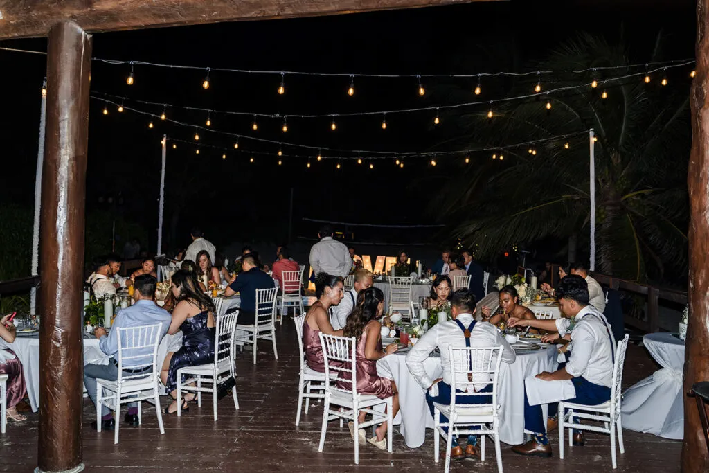 Elegant wedding reception dinner under string lights at tropical Riviera Maya resort with guests celebrating outdoors