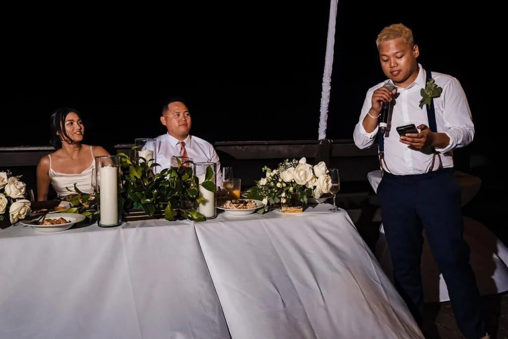 Wedding speech at outdoor Cancun reception with bride and groom at head table listening to best man toast